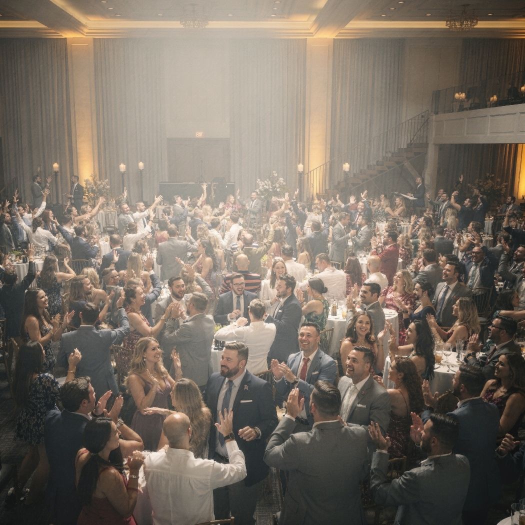 Large elegant banquet hall filled with well-dressed guests clapping and cheering at an event.