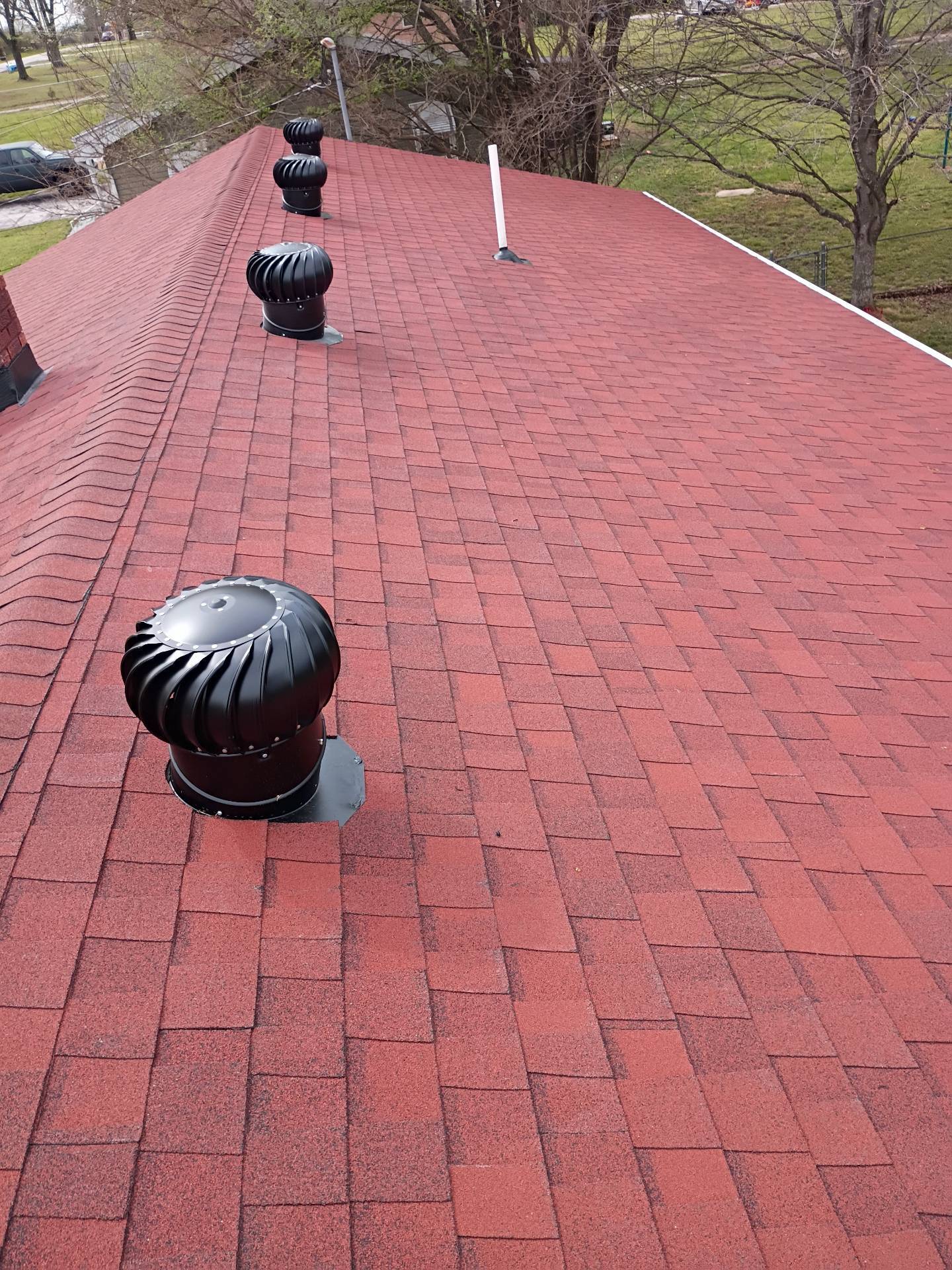 Worker in safety harness sealing a shingled roof with a caulking gun under a clear blue sky.