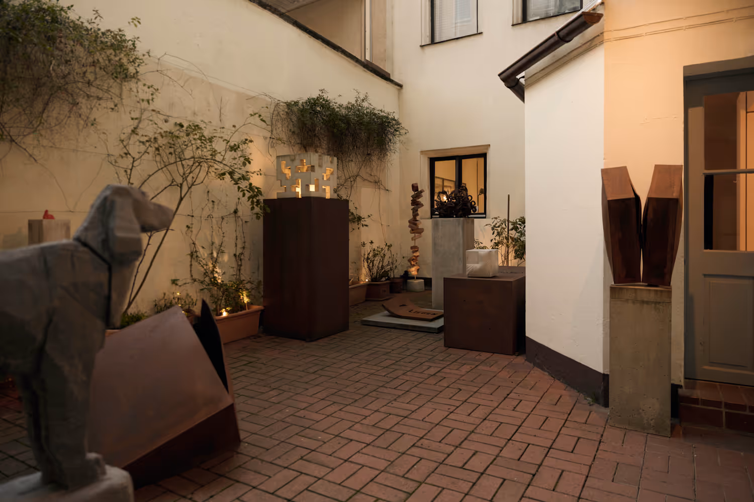 KunstKontor Nürnberg - Innenhof mit verschiedenen modernen Skulpturen auf Sockeln und Kletterpflanzen an den Wänden.