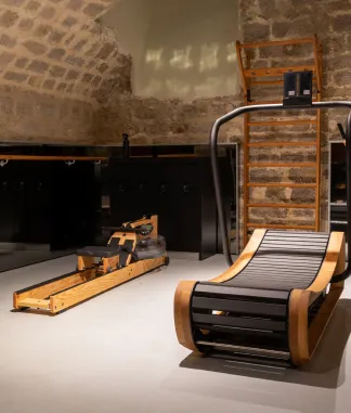 Salle de gym avec mur en pierre, appareil de rameur en bois et chaise de massage inclinée.