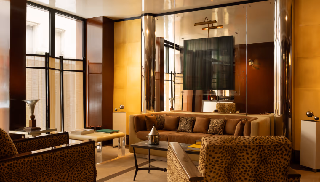 Salon d'hôtel élégant avec canapé beige, fauteuils à motif léopard et murs dorés réfléchissants.