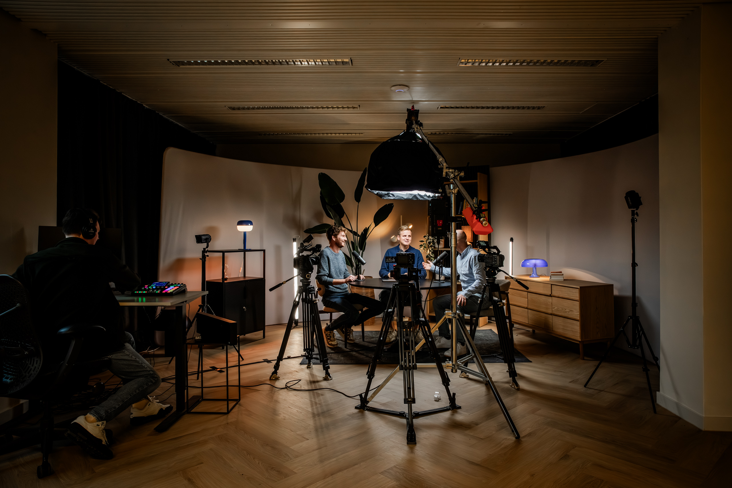 Blonde woman in black jacket speaking into a microphone during a podcast or interview with soft lighting in the background.