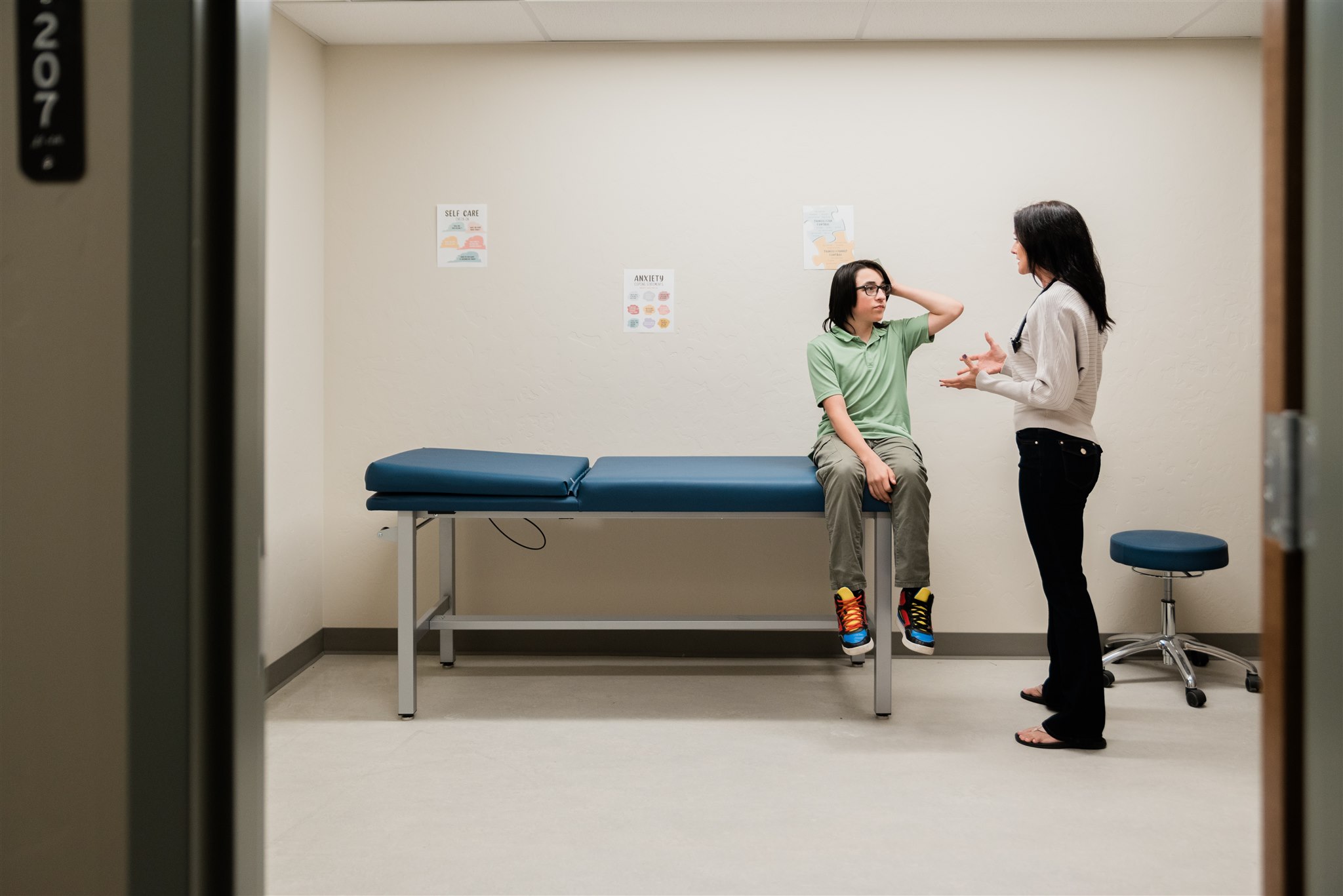 A nurse talks with a teen sitting on an exam table in a bright medical room at the Residential Center