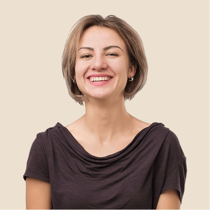 Smiling woman with short brown hair wearing a dark purple top against a beige background.