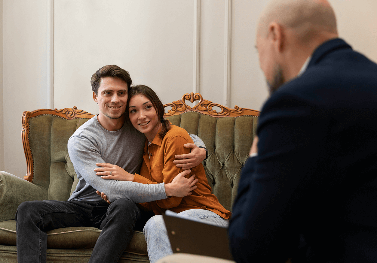Young couple sitting closely and hugging on a vintage green sofa during a counseling session with a therapist.