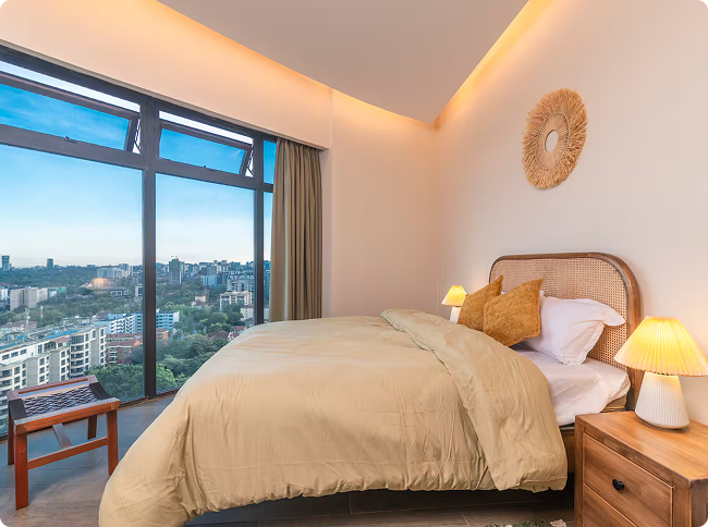 Modern bedroom with large window, beige bedding, two orange pillows, bedside lamp, and wooden nightstand.