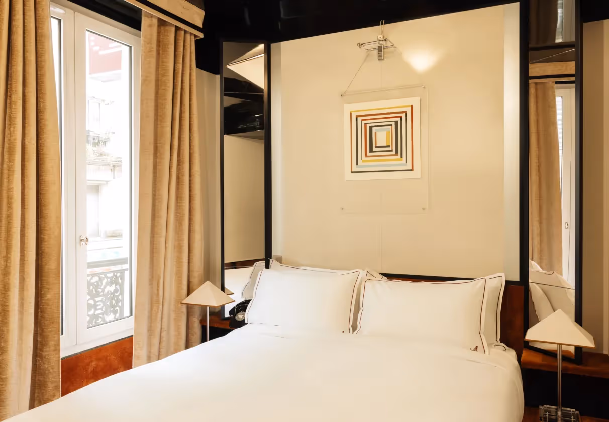 Refined interior of the Hôtel Château d’Eau, a 4-star hotel in Paris. The room blends seventies style, crisp white linens, modern bedside lamps, and elegant curtains.