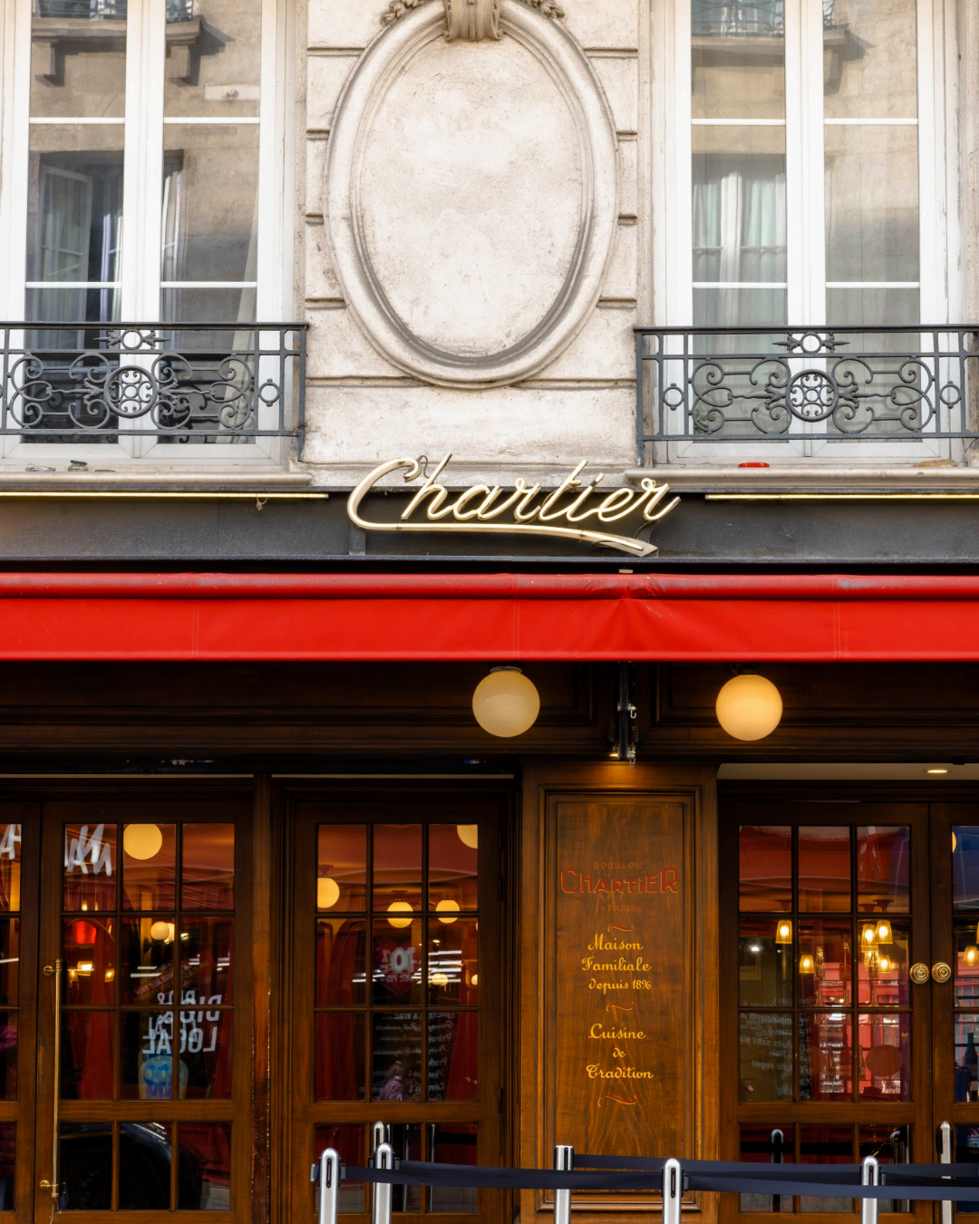 Façade du restaurant Chartier à Paris : enseigne dorée en lettres cursives, auvent rouge et devanture en bois avec vitrines lumineuses.