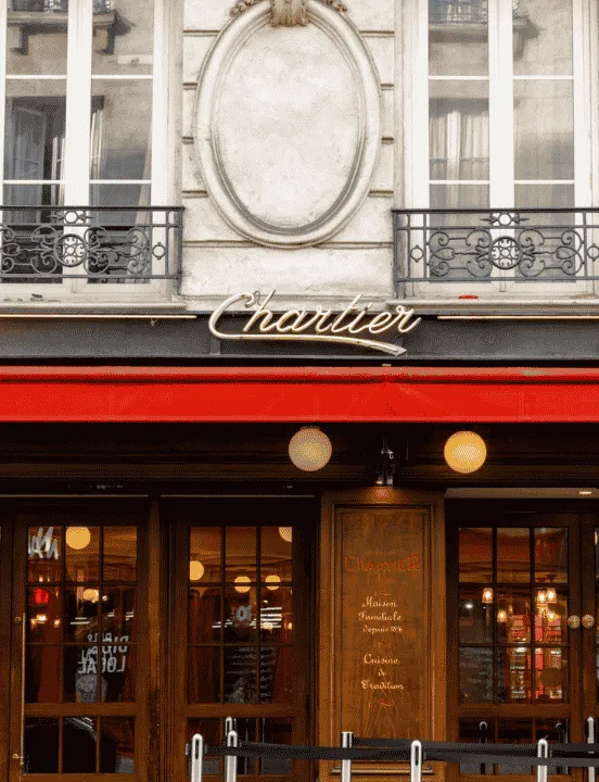 Façade du restaurant Chartier à Paris : enseigne dorée en lettres cursives, auvent rouge et devanture en bois avec vitrines lumineuses.