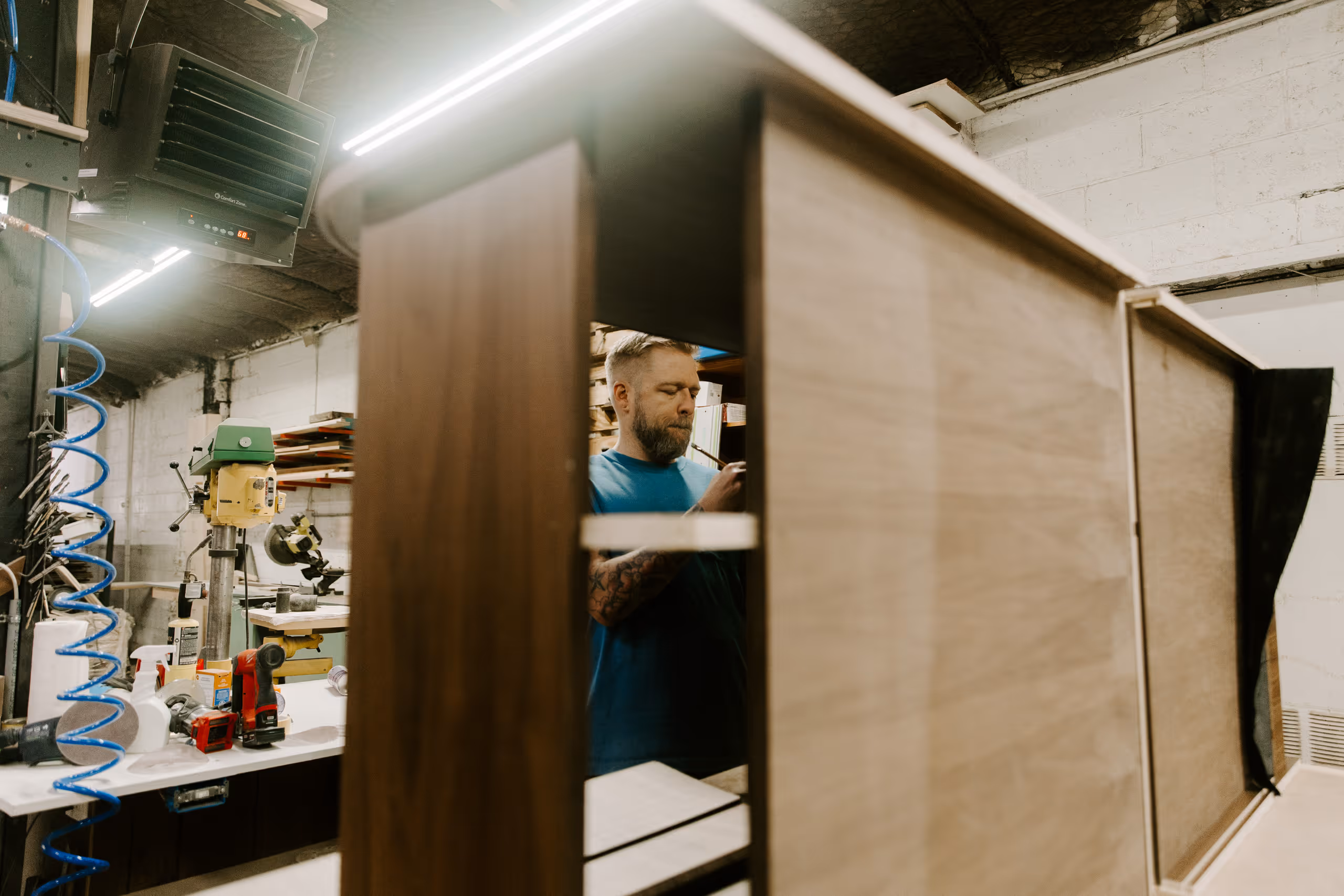 Man working with custom wooden cabinetry in a workshop filled with tools and equipment.