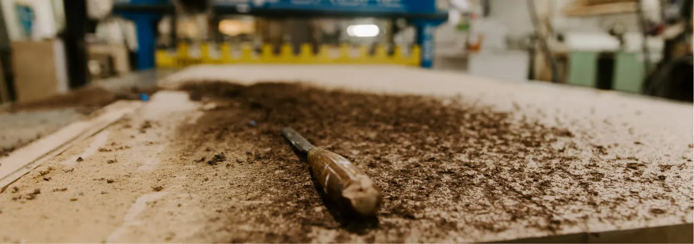 Wood chisel lying on a wood surface covered with wood shavings in a woodworking shop.