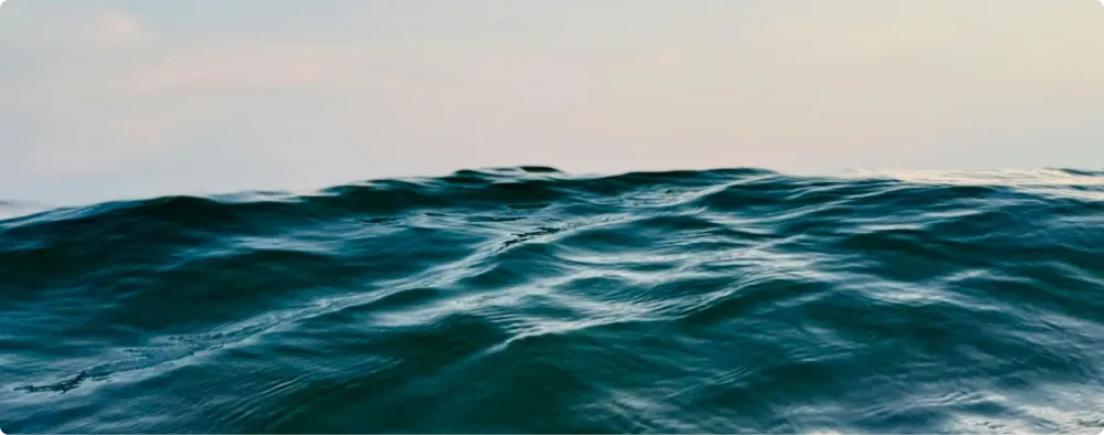 Close-up of ocean waves under a cloudy sky at horizon.
