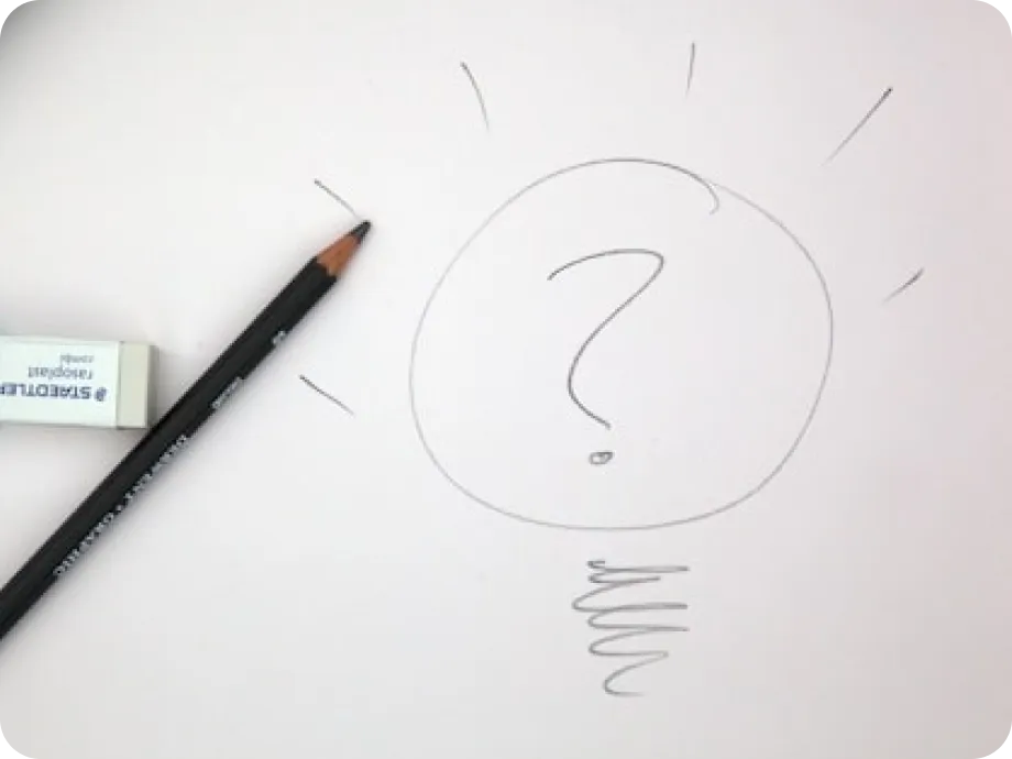 Pencil and eraser next to a hand-drawn light bulb with a question mark inside on white paper.
