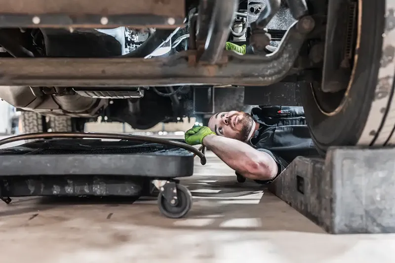 Pre-trip inspection of a heavy-duty truck as a technician checks underneath the vehicle for maintenance issues.