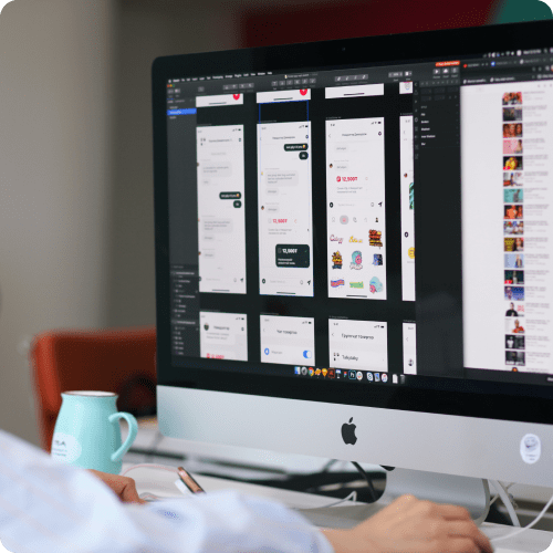 Person working on a desktop computer displaying multiple screens of mobile app design prototypes in a design software interface.