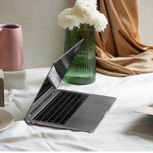 un ordinateur presque fermé  sur une nappe blanche et un petit bocale avec des fleurs blanche dedans  , une image décorative 