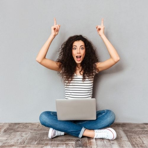 une fille assise en tailleur avec un pc sur les jambes qui leve les mains en l'air