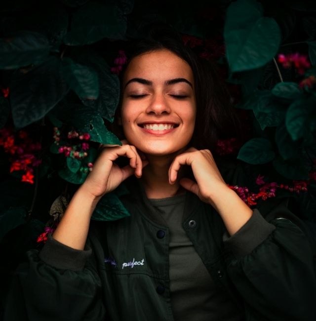 une jeune femme souris entouré de plantes et de fleurs