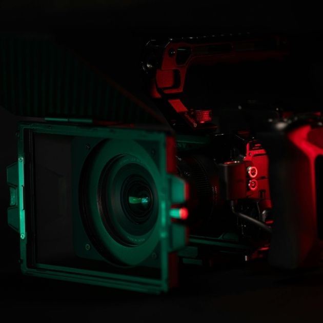 Caméra vidéo professionnelle de cinéma avec éclairage studio rouge et vert sur fond noir, symbolisant la création de contenu vidéo haute performance aux Sables-d'Olonne.