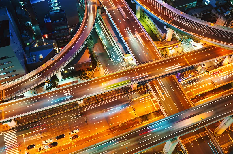 Aerial view of a complex multi-level highway interchange lit by streetlights at night with light trails from moving vehicles.