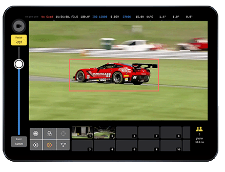 Tablet screen displaying a red race car on a racetrack being tracked by AI auto-tracking software, showing camera settings and focus on the car with a red tracking box.