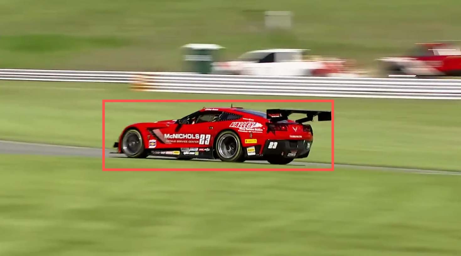 Tablet screen displaying a red race car on a racetrack being tracked by AI auto-tracking software, showing camera settings and focus on the car with a red tracking box.