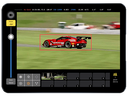 Tablet screen displaying a red race car on a racetrack being tracked by AI auto-tracking software, showing camera settings and focus on the car with a red tracking box.