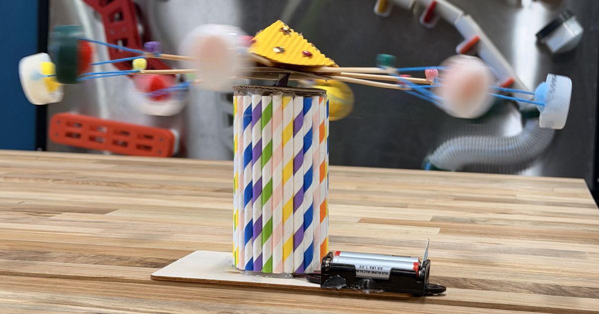 Colorful homemade spinning carnival ride model made from paper straws, craft materials, and a battery-powered motor on a wooden table.