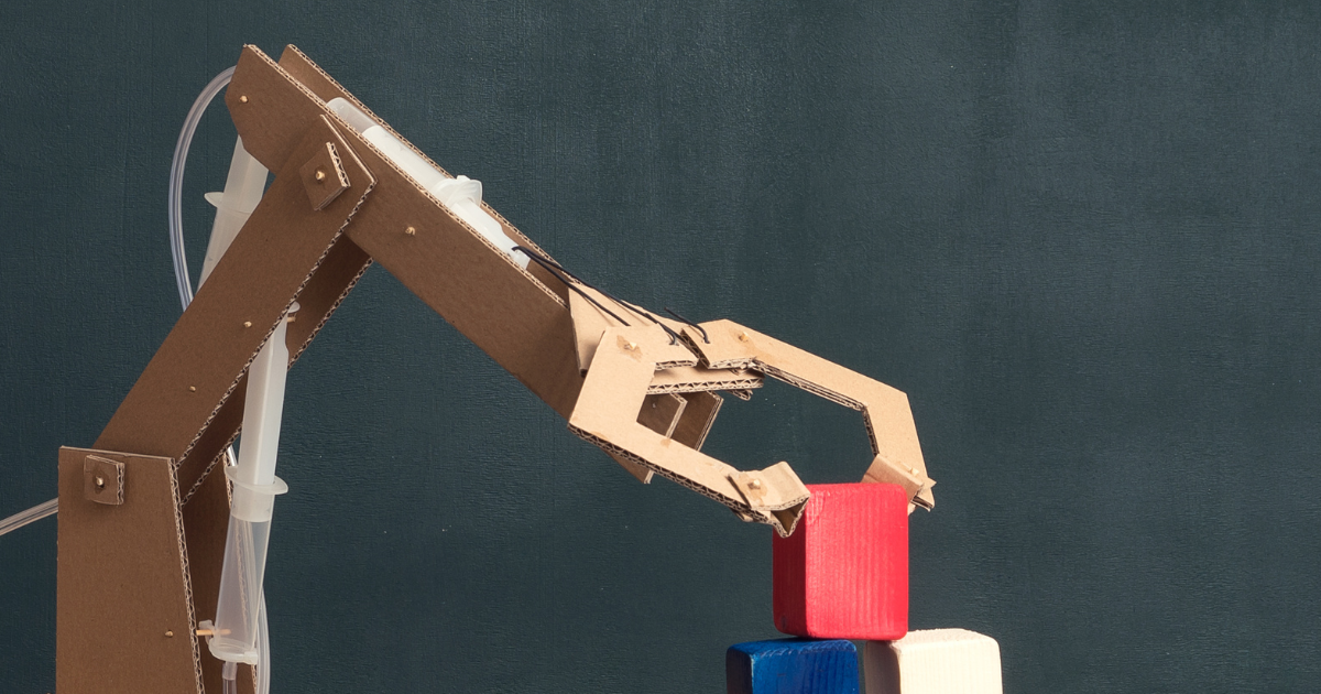 Cardboard hydraulic robotic arm lifting a red block, demonstrating engineering and mechanical movement through a hands-on STEM project.