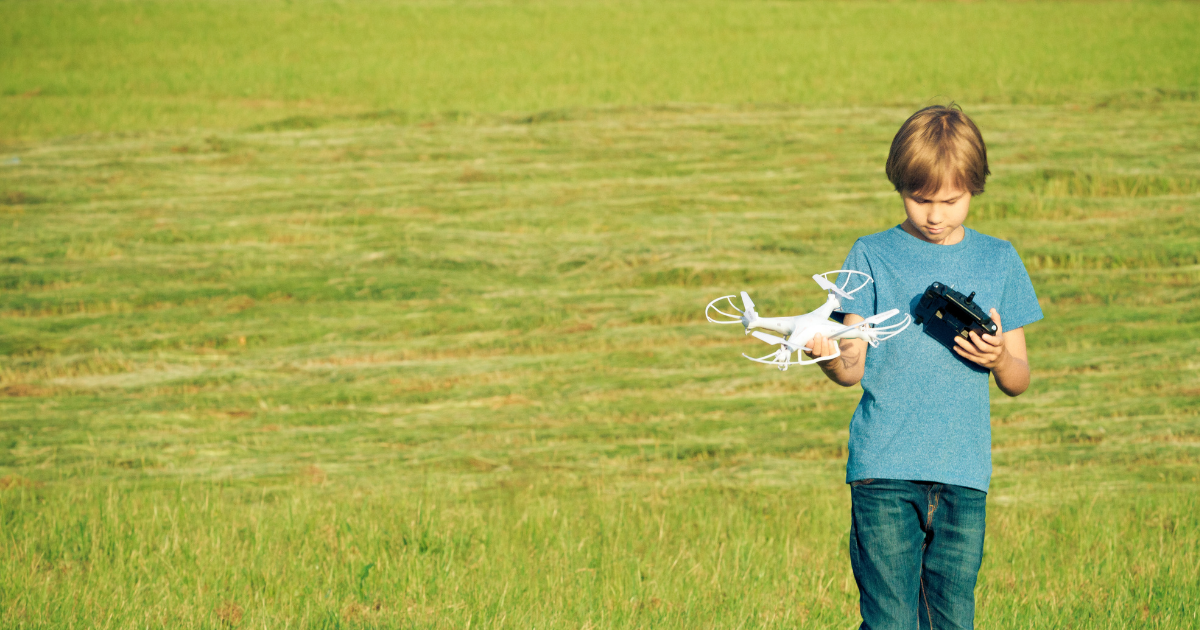Young camper standing in a grassy field holding a drone and controller while preparing for a hands-on flight and engineering activity.