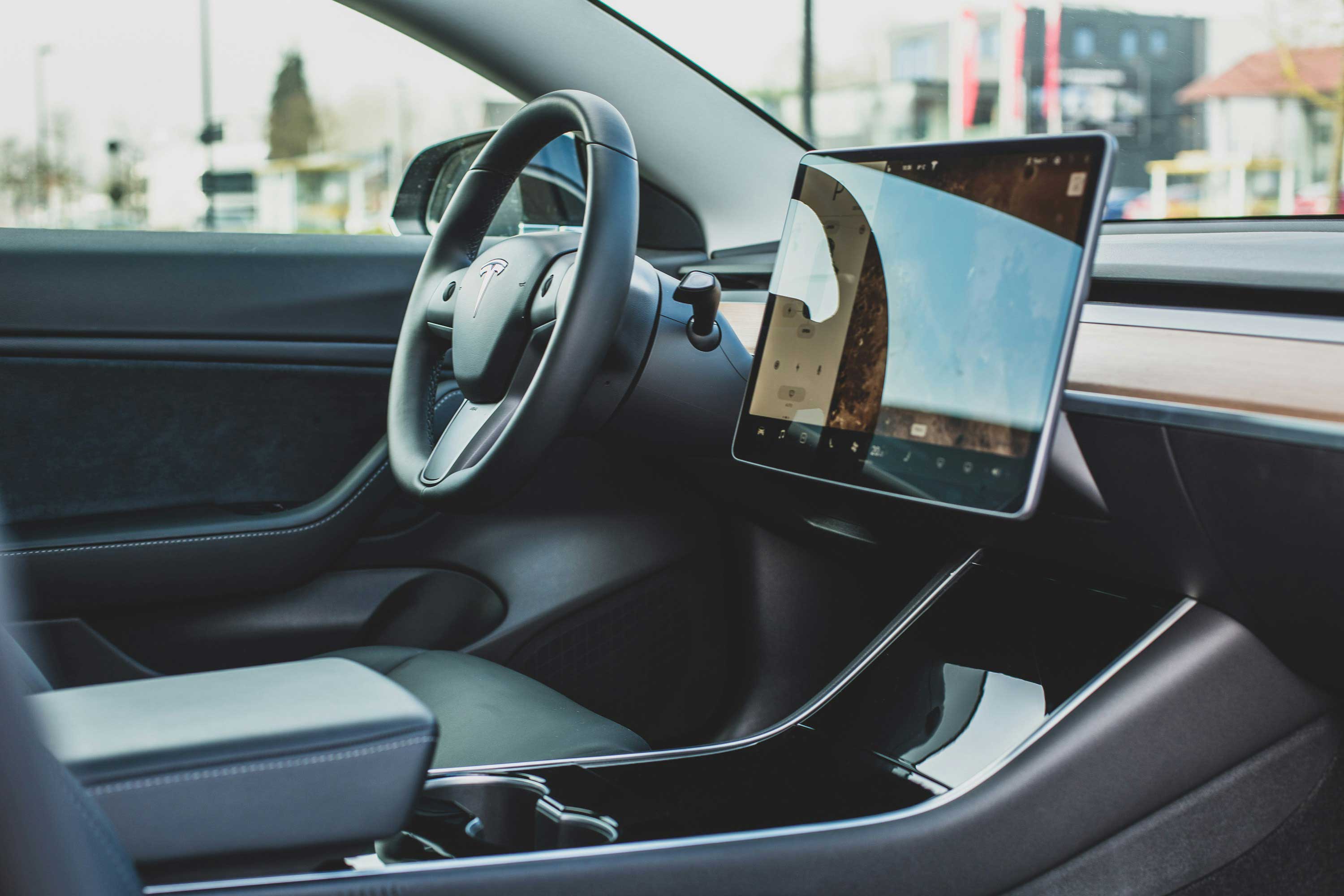 Interior of a Tesla car showing the steering wheel and a large touchscreen display on the dashboard.
