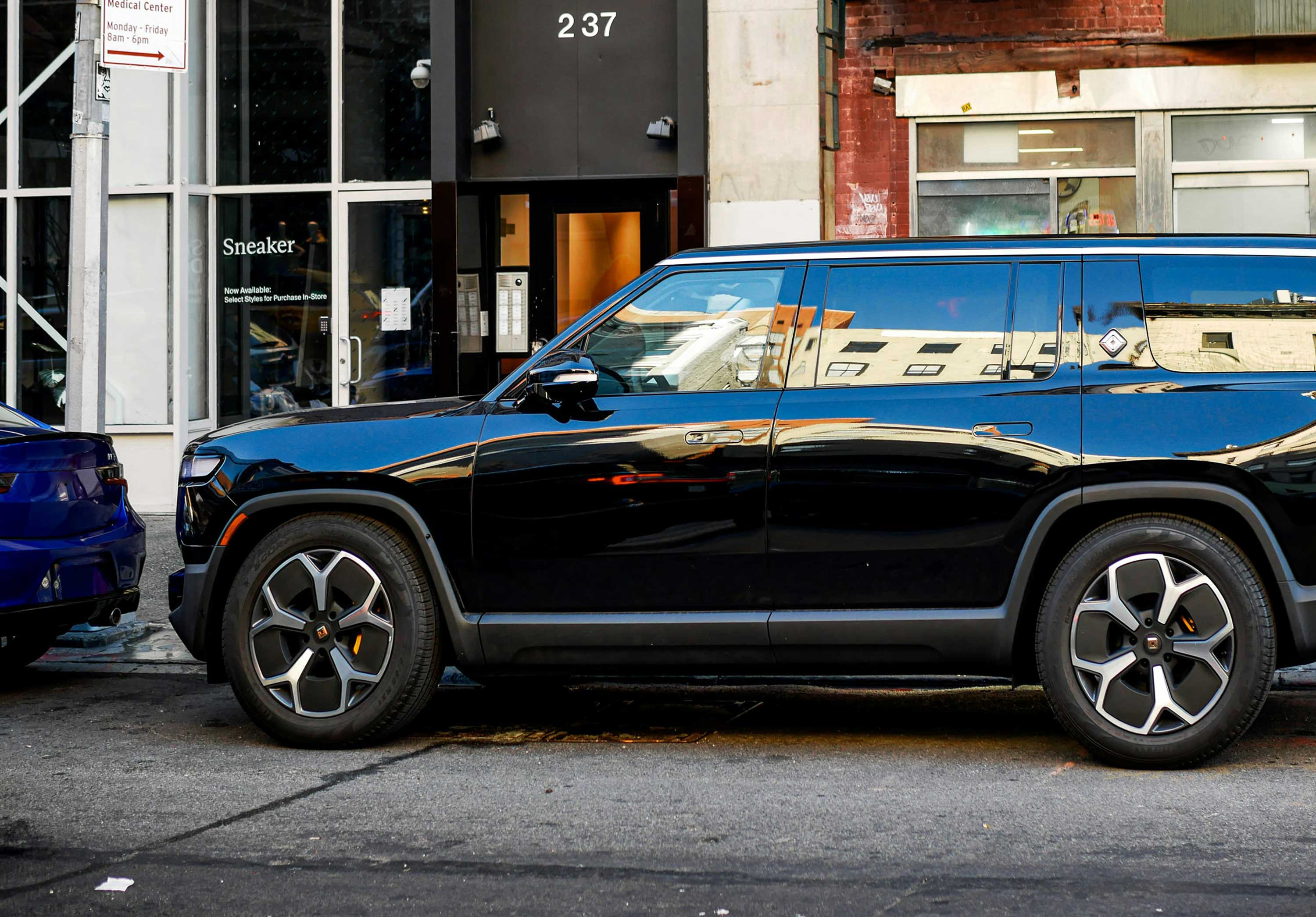 Black modern SUV parked on a city street with buildings reflected on its windows.