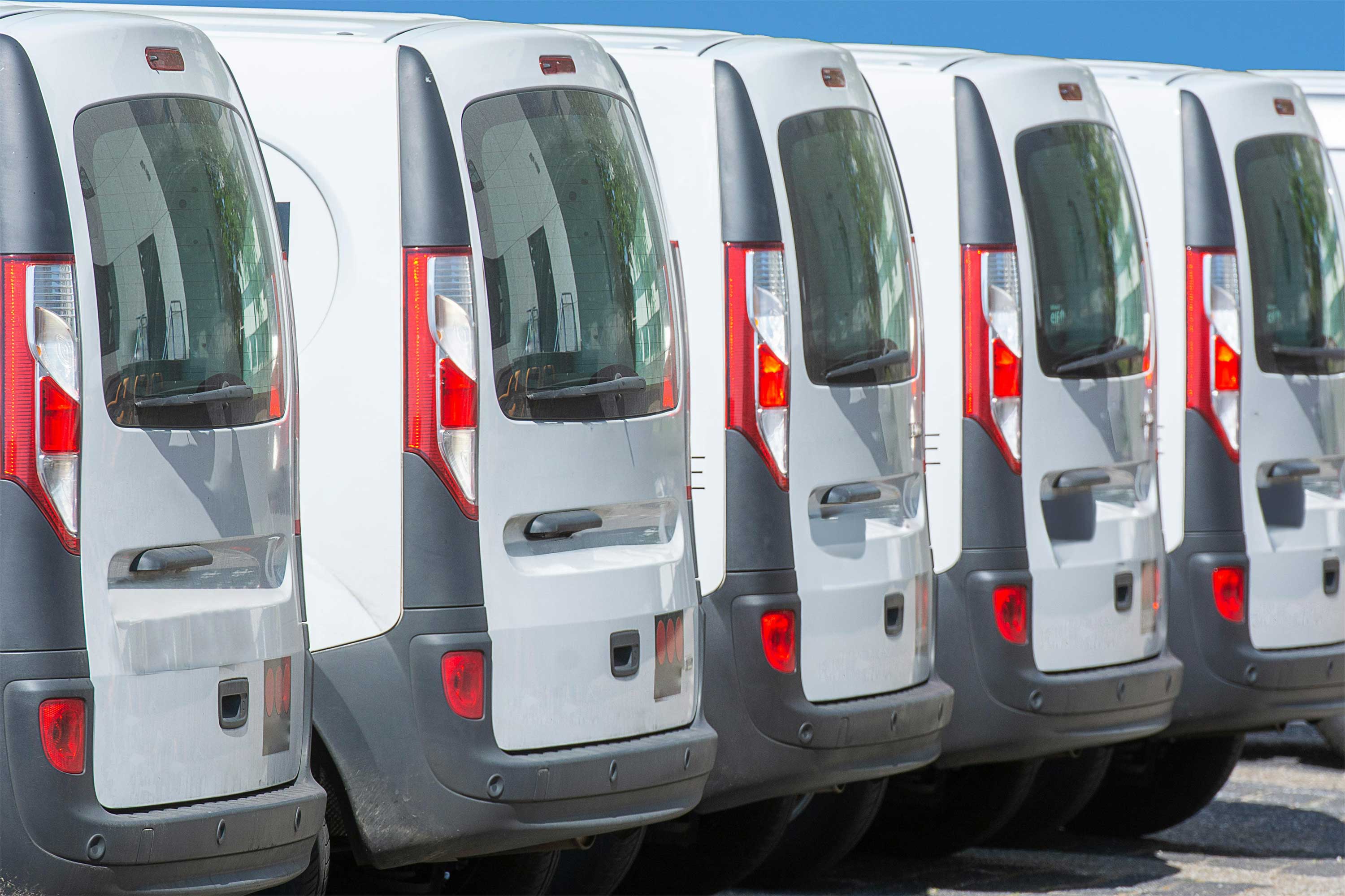 Row of white delivery vans parked side by side under a clear blue sky.