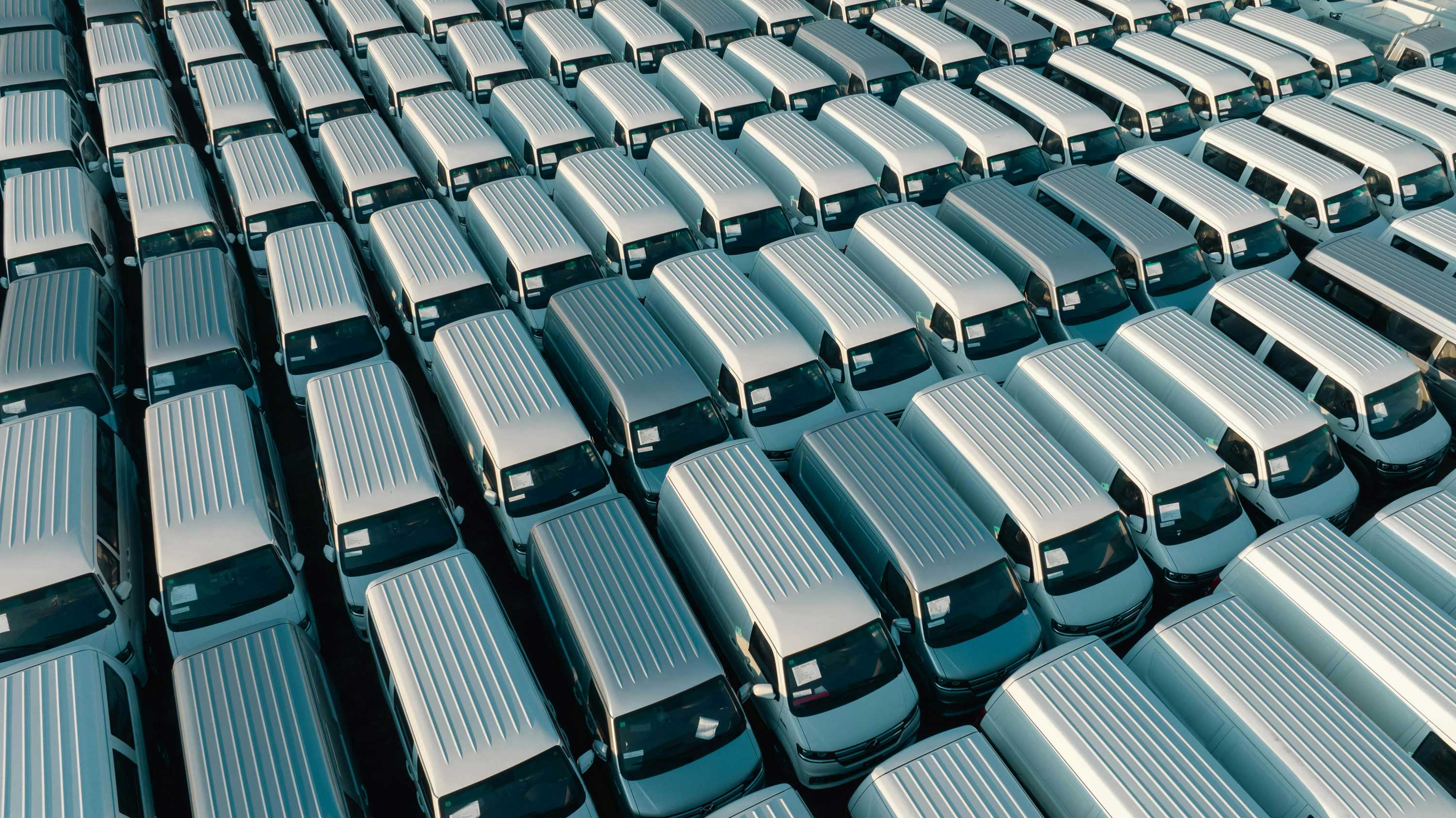 Rows of white passenger vans parked tightly together in an outdoor lot.