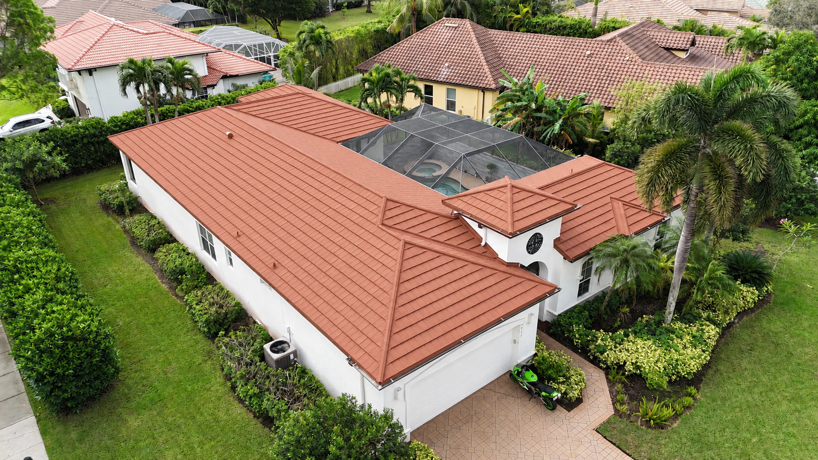 Aerial view of a white house with a red tiled roof and a screened pool in a green yard.