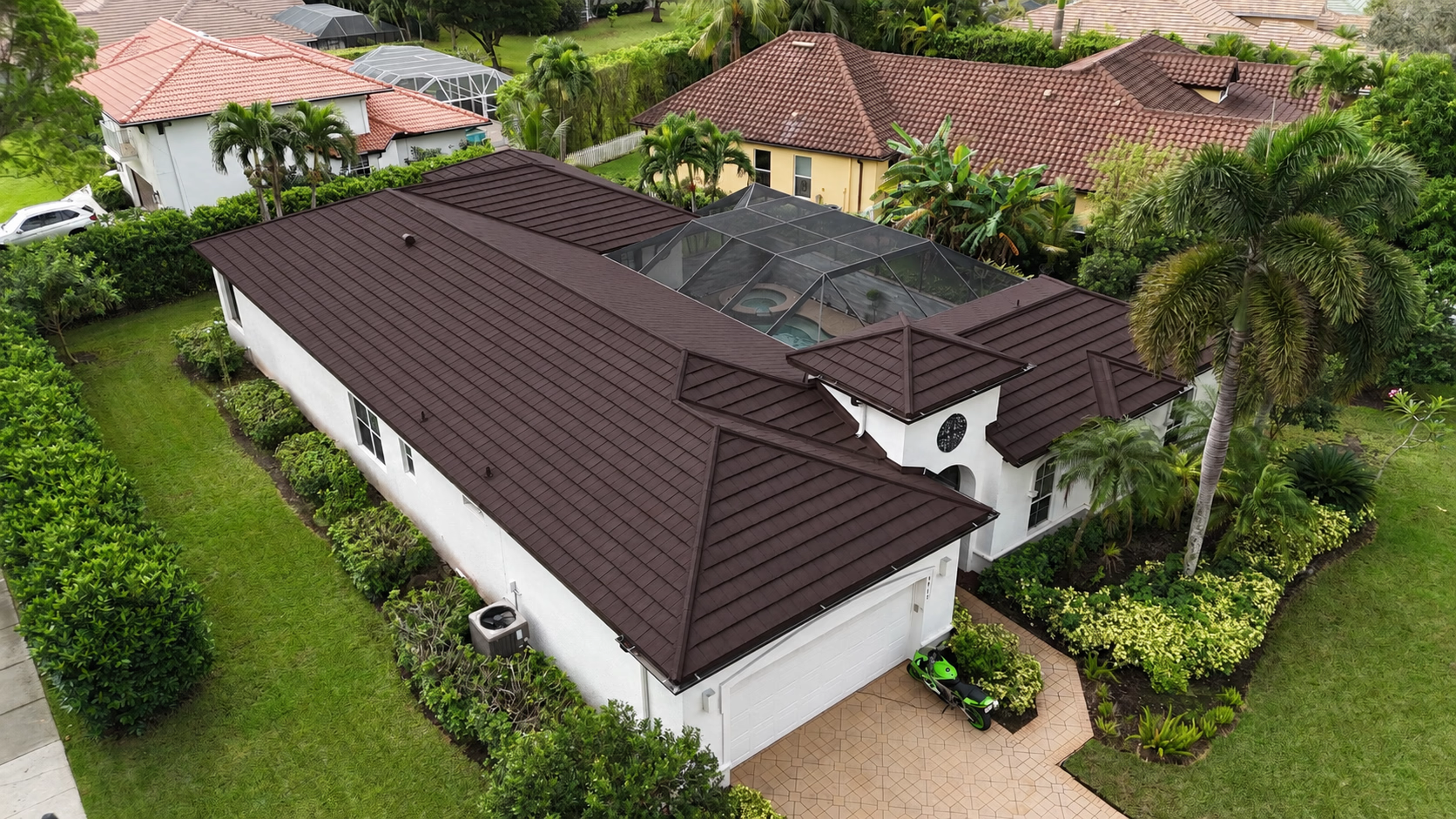Aerial view of a single-story house with a dark brown metal tile roof and screened pool area.