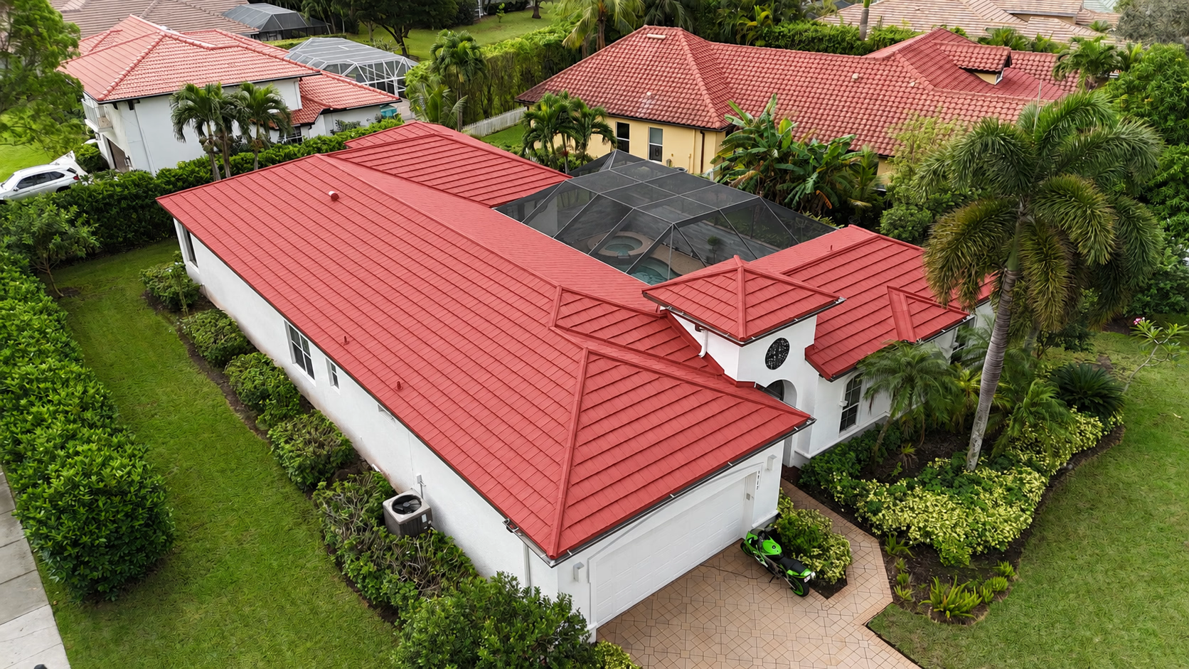 Aerial view of a white house with a red tiled roof and a screened pool enclosure in the backyard.