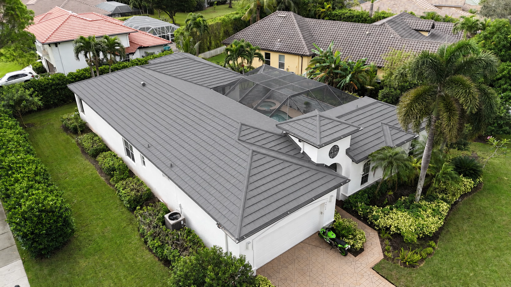 Aerial view of a white single-story house with a gray tiled roof and screened pool in backyard.
