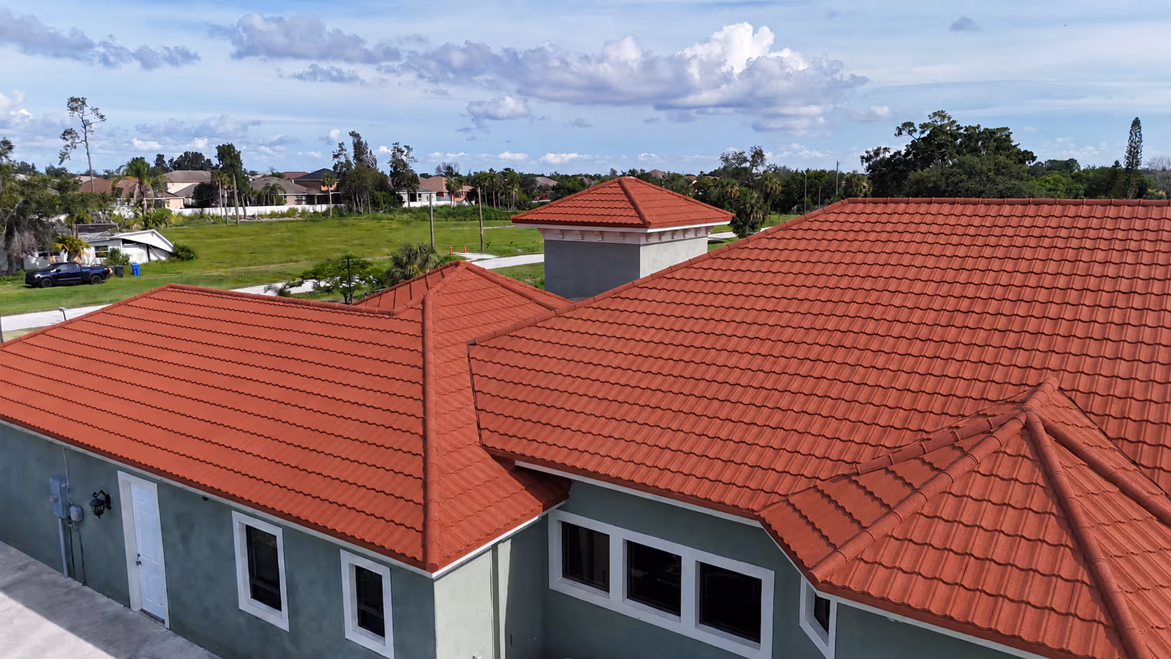Red tiled roof on a green house with white framed windows under a partly cloudy sky.