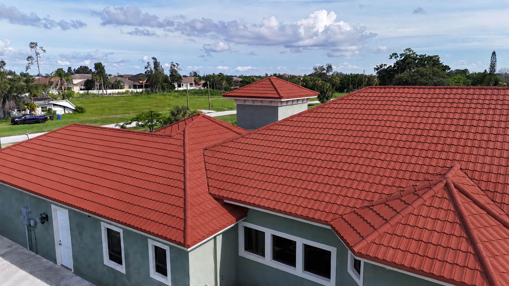 Red tiled roof on a green house with white framed windows under a partly cloudy sky.