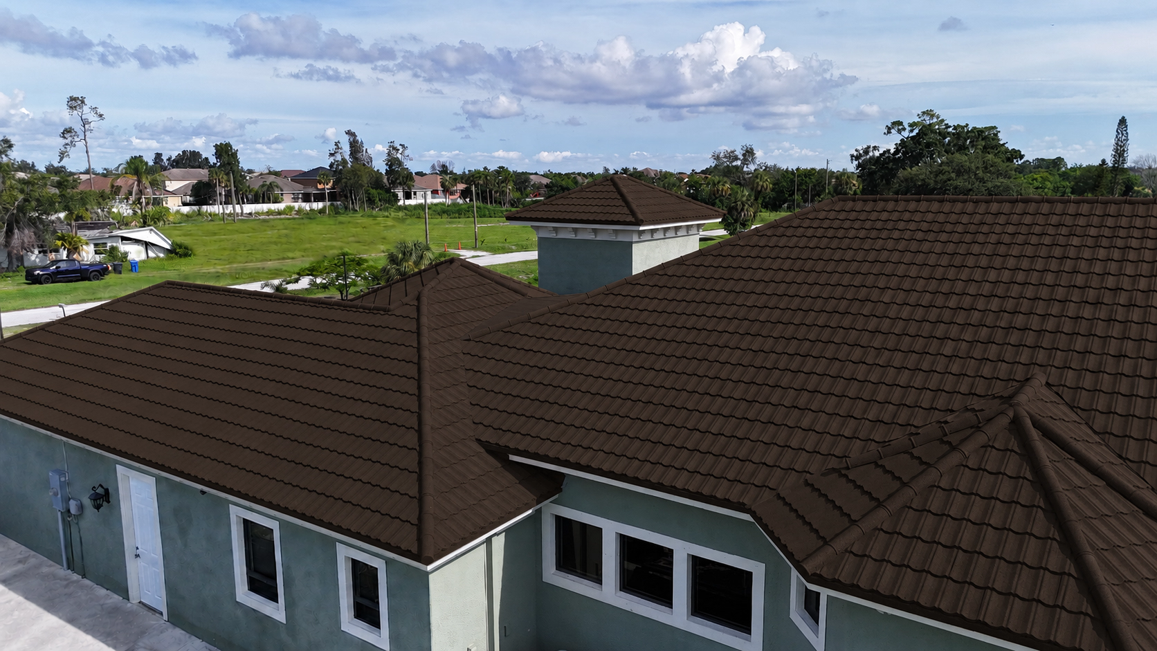 House with dark brown metal tile roofing and a green exterior wall under blue sky.