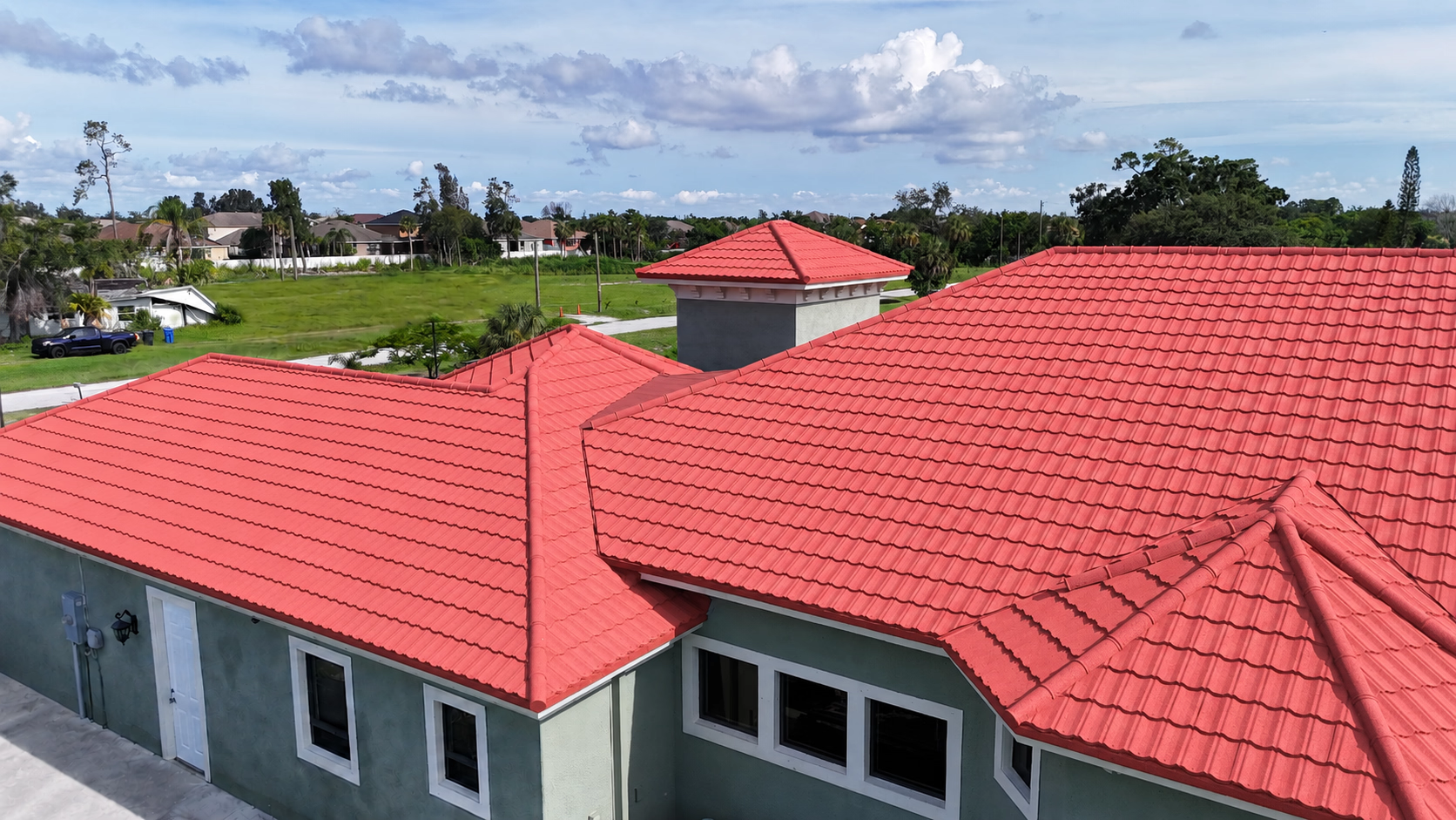 House with a red tile roof under a partly cloudy sky with greenery in the background.