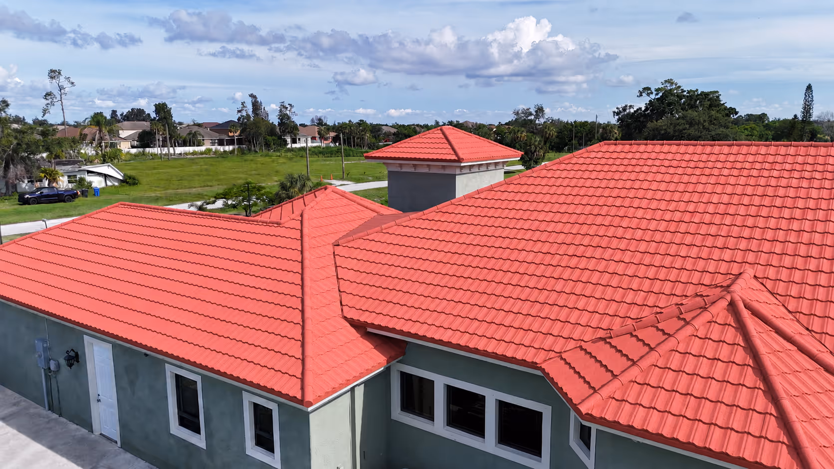 House with a red tile roof under a partly cloudy sky with greenery in the background.