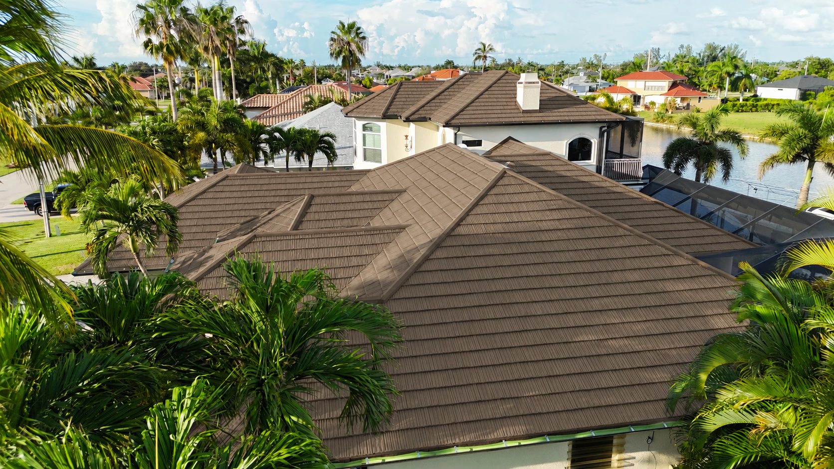 Aerial view of houses with brown tiled roofs surrounded by palm trees in a sunny neighborhood.