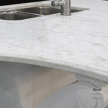Close-up of a white marble kitchen countertop with a beveled edge and a stainless steel sink with faucet.