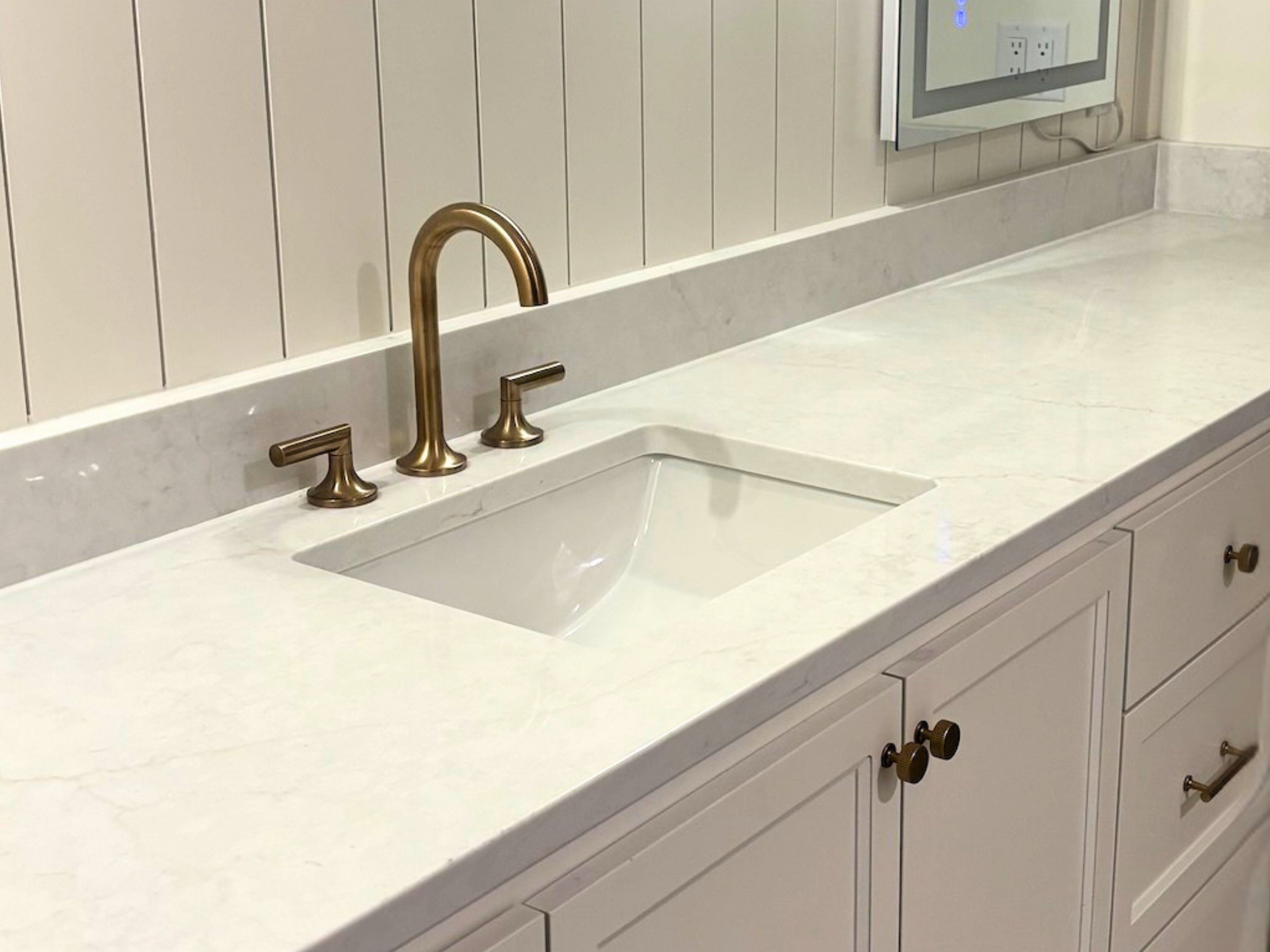 Modern bathroom countertop with a white quartz surface, integrated sink, and brushed gold faucet and handles.