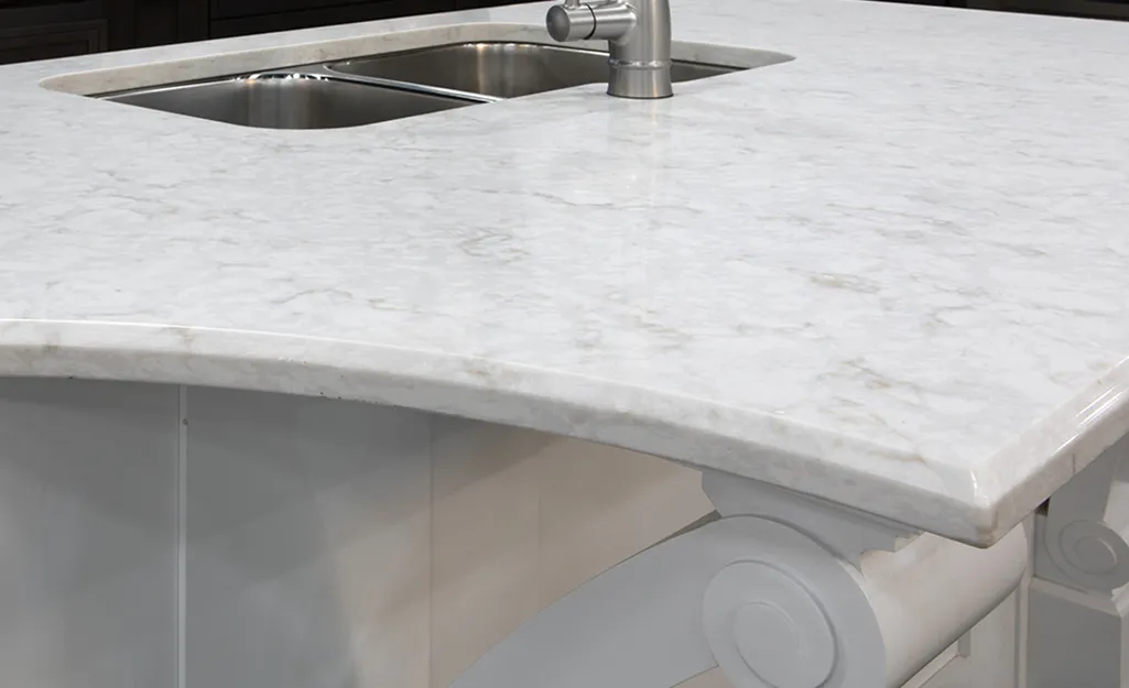 White marble kitchen countertop with beveled edges, integrated double sink, and chrome faucet.
