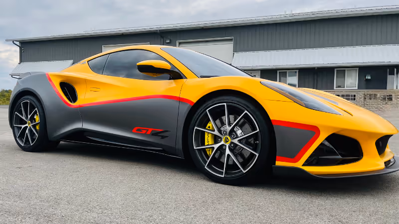 A striking yellow sports car with gray accents and red detailing, parked on a smooth surface. The car features sleek lines and a modern design, showcasing its stylish profile near a gray building.