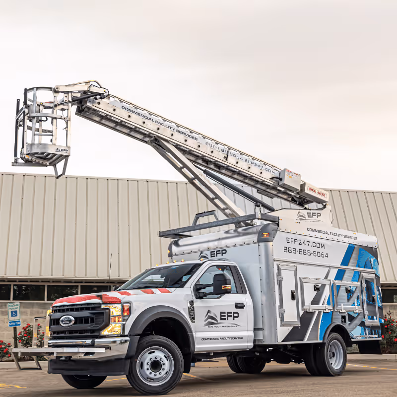 A specialized service truck with an extended aerial lift equipped with a basket, parked outside a building. The truck features a modern design with blue and white graphics, displaying the logo and contact information for EFP services.