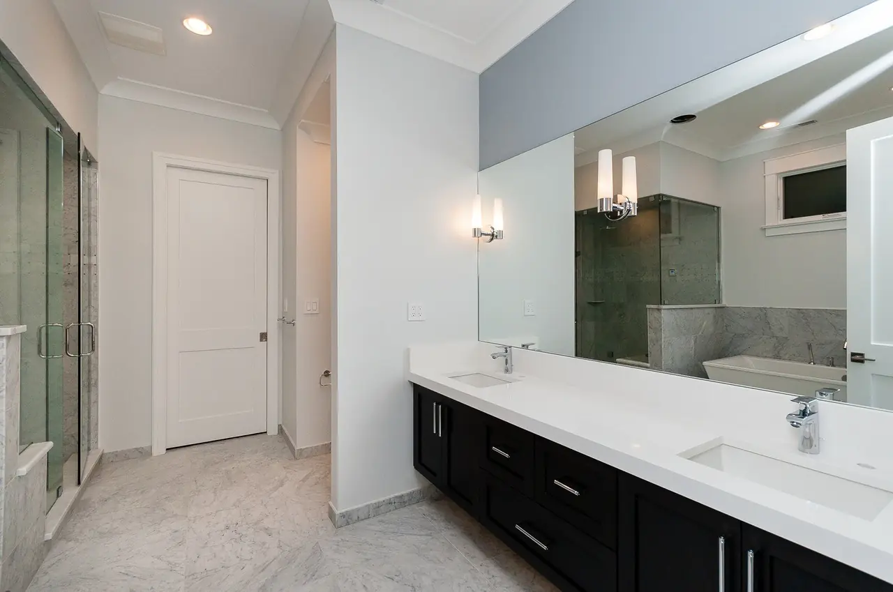 Bathroom hallway with a dark wood double vanity and a mirror reflecting the walk-in shower.